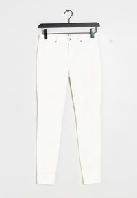 White slim-fit jeans with front button, belt loops, and five pockets hanging on a black plastic hanger against a white background.