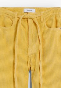 Żółte spodnie z kordurojowej tkaniny z regulowanym paskiem w pasie, dwiema przednimi kieszeniami i pionową fakturą ribbingu. Metka głosi "SCALPERS."