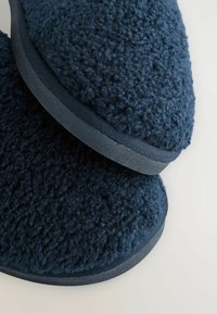 Marinblå tofflor med ett mjukt, fluffigt material; rundad form; texturerad ovansida; avslutade med en hållbar, slät gummisula.