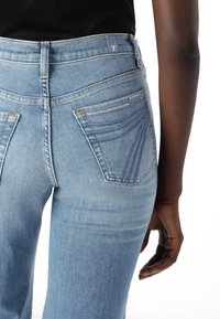 Jeans de culoare albastru deschis, cu talie înaltă și o formă ajustată. Prezintă două buzunare pe spate cu detalii de cusătură subtilă și închidere cu un buton metalic.