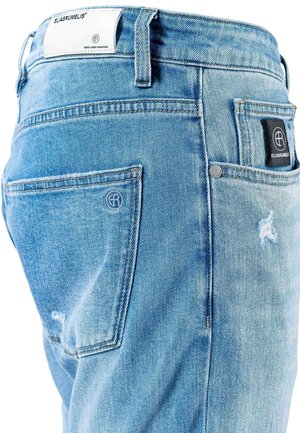 Lys blå denimbukser med en falmet tekstur, som har en baklomme med en svart etikett og logo, samt slitte detaljer på stoffet.