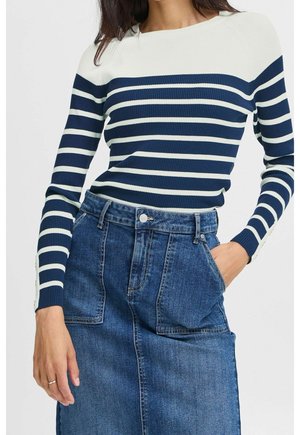 Femme portant un pull rayé bleu marine et blanc à manches longues et une jupe en jean bleu taille haute avec de grandes poches devant.