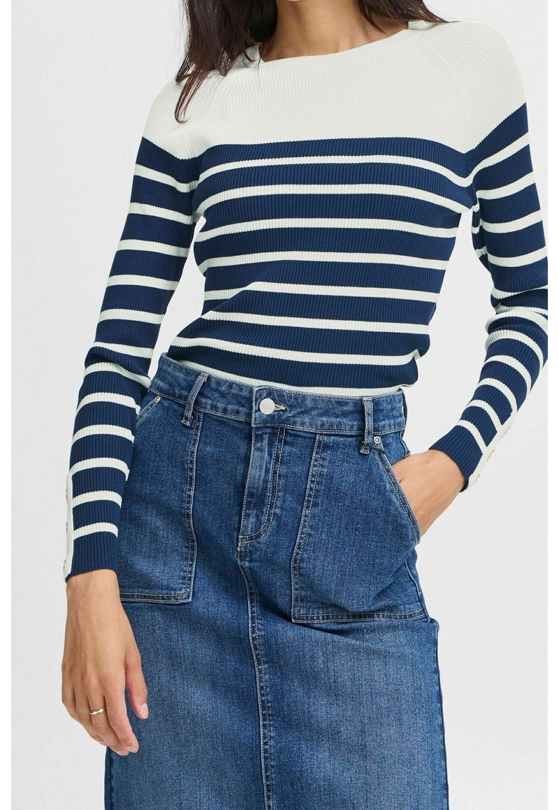 Femme portant un pull rayé bleu marine et blanc à manches longues et une jupe en jean bleu taille haute avec de grandes poches devant.