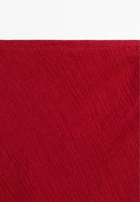 Czerwona tkanina o fakturze z delikatnymi skośnymi zagnieceniami i złożonym brzegiem u góry na białym tle.