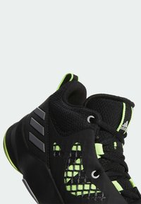 Baskets montantes Adidas noires et vert néon avec panneaux en mesh, lacets et trois bandes grises sur le côté.