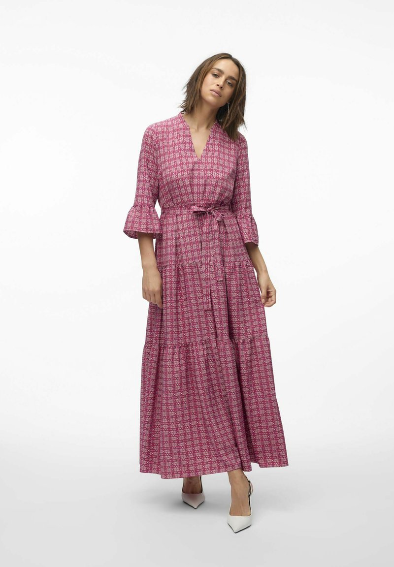 Robe longue rose avec motif floral, décolleté en V et manches évasées. Elle dispose d'une taille cintrée avec un lien et d'un design de jupe à volants.