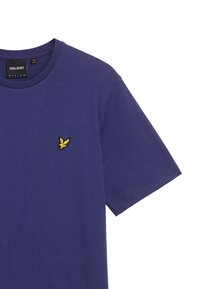 T-shirt di cotone viola con scollo tondo e maniche corte. Presenta un piccolo logo ricamato giallo sul petto. Tessuto morbido.