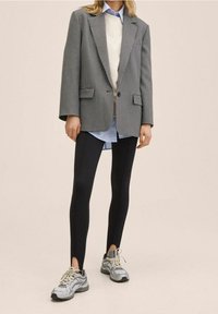 Szary żakiet w grafitową kratę, pod nim biały sweter, jasnoniebieska koszula, czarne legginsy oraz szare sneakersy z białymi akcentami.