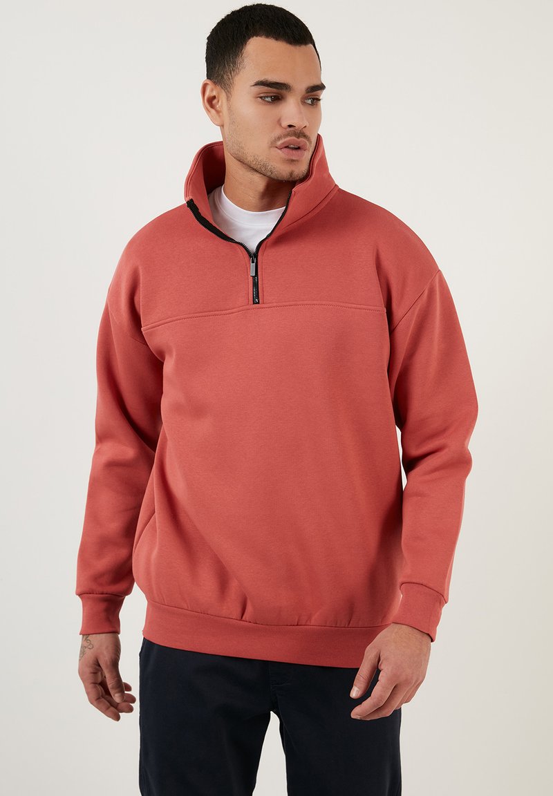 Fleece pullover in coraal met een kwart-rits kraag. Heeft een horizontale naad over de borst en ribbronzen manchet. Zachte textuur.