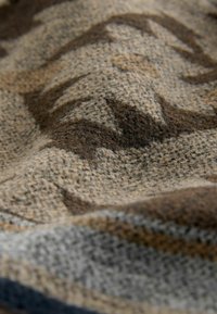Primo piano di un tessuto a maglia testurizzato con un motivo di strisce zigzag marroni, beige e grigie.