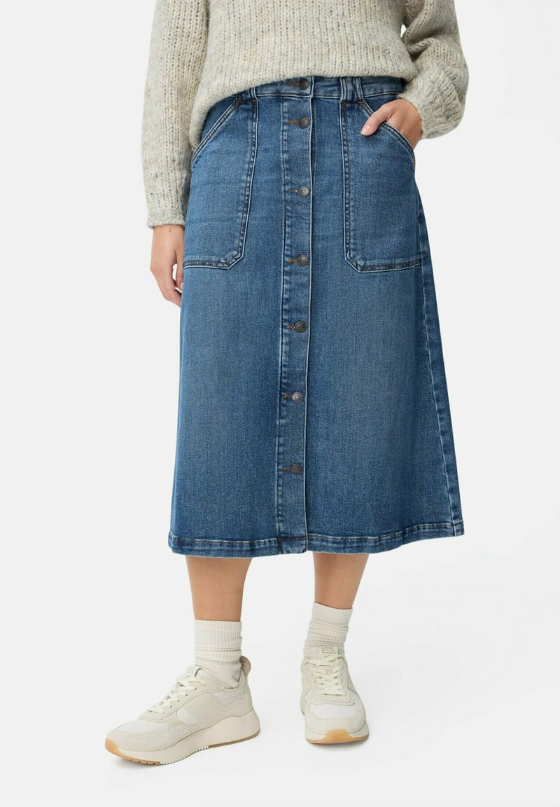 Jupe midi en denim bleu foncé avec un devant boutonné, deux poches avant et un ourlet juste en dessous du genou. Associée à des baskets blanches.