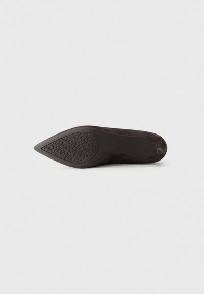 Chaussure plate noire en suede à bout pointu vue du dessous, avec une semelle texturée et un petit talon, sur fond gris clair.