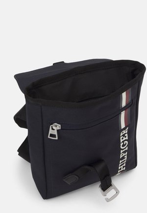Lille mørkeblå skuldertaske med frontlynlåslomme, delvist åben hovedrum, stribet detalje og mærkenavn "Hilfiger" på siden.