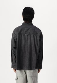 Camicia in denim scuro con maniche lunghe, polsini con bottoni e colletto classico. Presenta un giogo posteriore e una vestibilità ampia e rilassata.