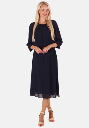 Marineblaue Midikleid mit Dreiviertelärmeln, gefaltetem Ausschnitt und elastischem Bund. Leichter Stoff, halbtransparenter Saum. Getragen mit nudefarbenen Sandalen.
