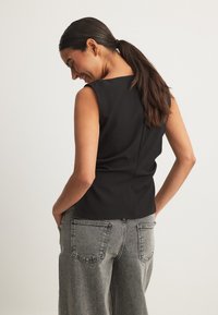 Mustõttu must särk, millel on istuv siluett, tekstuurne kangas ja sile seljaosa, kombineeritud kõrge vöökohaga hallide teksapükstega.