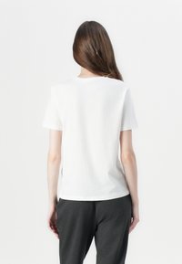 Hvid bomulds t-shirt med korte ærmer og rund halsudskæring, parret med grå bukser. Enkel design, glat tekstur, ingen mønstre eller accenter.