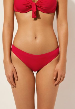 Bikini rouge avec un haut noué et un bas à couverture minimale et lisse. Le matériau semble élastique et doux, de couleur unie et sans motifs.
