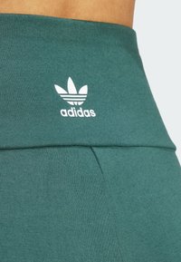 Teal športové legíny s hladkou textúrou, s širokým pásom a bielym logom Adidas a dizajnom trojlístka na prednej strane.