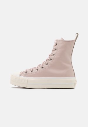 Hoge sneaker van pastelkleurig roze leer met witte dikke rubberen zool en neuskap, metalen veteroogjes en een treklipje aan de hiel.