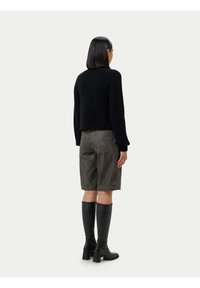 Svart, texturerad, kort tröja kombinerad med grå denimshorts och svarta knähöga stövlar med klack, sedd bakifrån mot en ljus bakgrund.