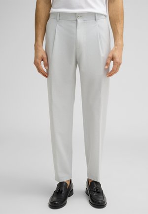 Light gray tailored trousers with a textured fabric, featuring pleats, side pockets, and a button closure, paired with black loafers.