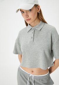 Grå kort polo skjorte med korte ærmer, prydet med en spids krave og tre knapper, iført med lysegrå stribede sweatpants.