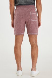 Shorts de color rojo jaspeado, elaborados en un material suave con una cinturilla de contraste, bolsillo trasero y costuras blancas. Combinados con zapatillas blancas.