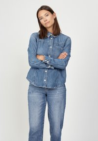 Blue denim shirt with a classic button-up design, chest pocket, and collar. Paired with matching light denim pants.