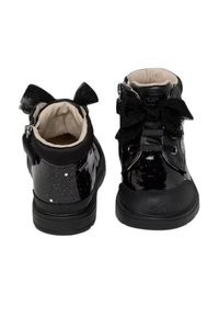 Stivaletti alla caviglia in pelle verniciata nera con fiocchi decorativi, fodera imbottita e suola in gomma testurizzata. Motivi a stella sul lato esterno.