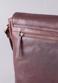 Brown leather bag with a zippered pocket, smooth texture, rectangular shape, and subtle stitching. Features a flap and metal hardware accents.