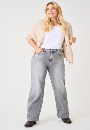 Grijze denim jeans met een relaxte pasvorm, gecombineerd met een wit T-shirt en een chunky, gebreide beige cardigan. Zwarte enkellaarsjes maken de outfit compleet.