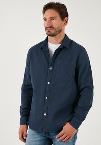 Camicia azzurra navy in cotone misto, con taschino sul petto, tessuto textured e bottoni a pressione argentati sul davanti.