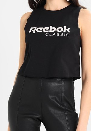 Kobieta w czarnym bezrękawniku Reebok Classic crop top i czarnych skórzanych spodniach z wysokim stanem, pokazana od szyi do bioder.