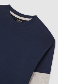 T-shirt in cotone blu navy con scollo rotondo, maniche corte e un accento grigio a contrasto lungo il bordo inferiore.