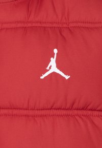 Rød polstret jakke med et hvidt broderet Jumpman-logo. Glat tekstur med stikninger for ekstra detalje.