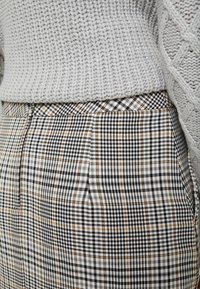 Pull en tricot gris avec un motif texturé, associé à un pantalon à carreaux noir, blanc et beige, doté de poches latérales et d'une coupe slim.