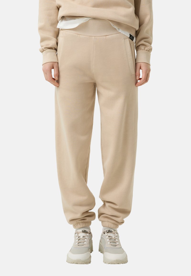 Beige sweatpants med en afslappet pasform, ribbede manchetter og sidelommer, parret med lyse sneakers. Glat stofstruktur.