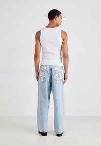 Hvit ermeløs topp, lyseblå vide jeans med broderte stjernemønstre og dekorative detaljer på lommene, båret med svarte sko.