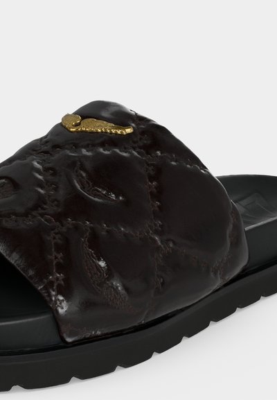 Μαύρο σανδάλι με δερμάτινο λουρί με υφή, με ανάγλυφα σχέδια και μια μικρή χρυσή λεπτομέρεια αλογάκι της θάλασσας στην κορυφή.