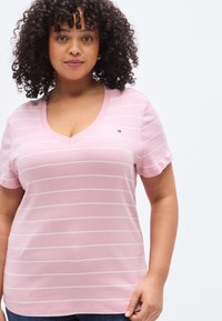 Ροζ βαμβακερό μπλουζάκι με λευκές οριζόντιες ρίγες, κοντά μανίκια και λαιμόκοψη σε σχήμα V. Μικρό λογότυπο της μάρκας στο αριστερό μέρος του στήθους.