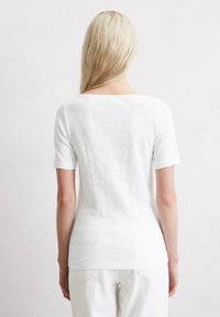 Hvid kortærmet skjorte med bred halsudskæring og slim fit. Lavet af et blødt, let materiale, den har en glat overflade og et minimalistisk design.