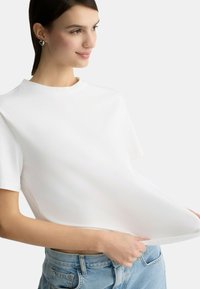 Maglietta bianca a maniche corte in morbido cotone, con scollatura a girocollo e vestibilità rilassata, abbinata a pantaloni corte a vita alta di colore azzurro chiaro.