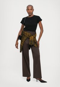 Black short-sleeve t-shirt, brown wide-leg trousers, and a patterned yellow and black scarf tied at the waist. Black pointed-toe heels.