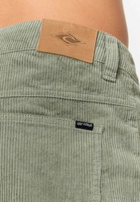 Gli shorts in velluto a coste verdi presentano una superficie testurizzata, una toppa in pelle con un logo e un'etichetta nera cucita. Hanno una vestibilità dritta e rilassata.