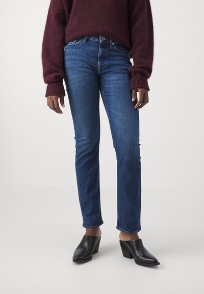 Vaqueros de mezclilla azul de corte ajustado, con cintura de altura media y un desvanecimiento sutil. Combinados con zapatos de tacón negros y un suéter texturizado burdeos.