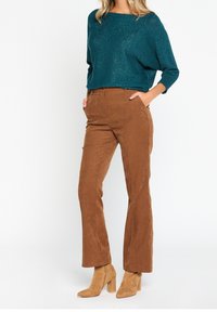 Teal glittrig tröja med vid halsringning, matchad med bruna kordfläskbyxor med vida ben och beige klackstövlar. Slät textur, avslappnad passform.