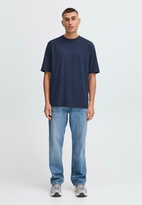 Marineblå bomulls t-skjorte med rund hals, korte ermer og ledig passform, kombinert med lyseblå jeans og grå sneakers.