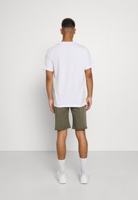 Vitt bomullströja och olivgröna shorts som bärs tillsammans. Outfits har en avslappnad passform, korta ärmar och en enkel design utan synliga mönster.