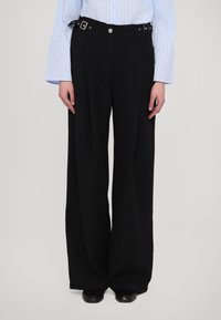 Zwarte wijde broek van soepel stof, voorzien van een tailleband met zilverkleurige gesp en een knoopsluiting.